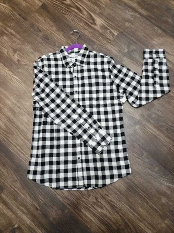 A black and white checkered shirt is laying on the floor.